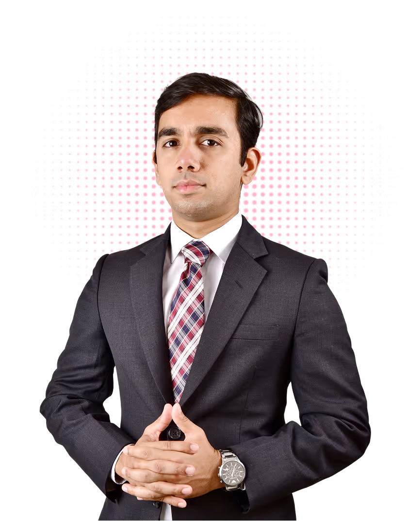 Young man in a dark suit with a white shirt and patterned tie, posing with clasped hands and a watch on his left wrist, against a background with pink dot pattern.