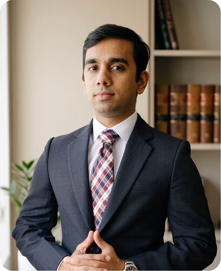 Confident man in dark suit and plaid tie standing in front of bookshelf with legal books.