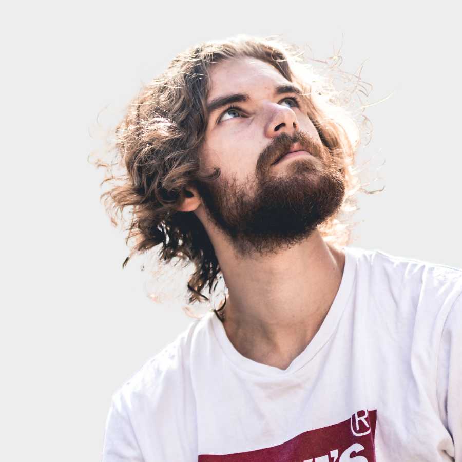 Young man with curly hair and beard looking upward wearing a white shirt with a red logo.