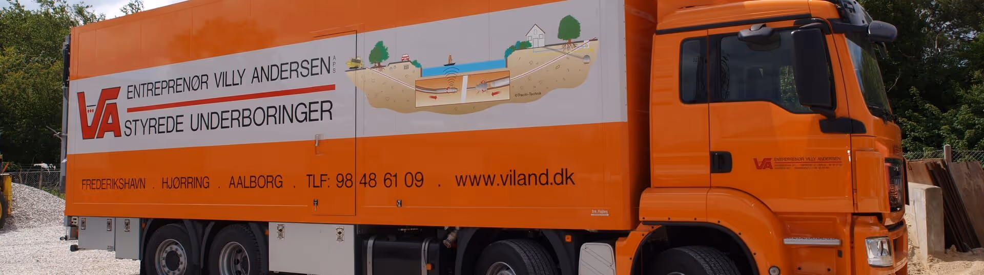 Orange truck with text advertising Entreprenør Villy Andersen APS and controlled horizontal directional drilling services, showing contact info and a diagram of underground drilling.