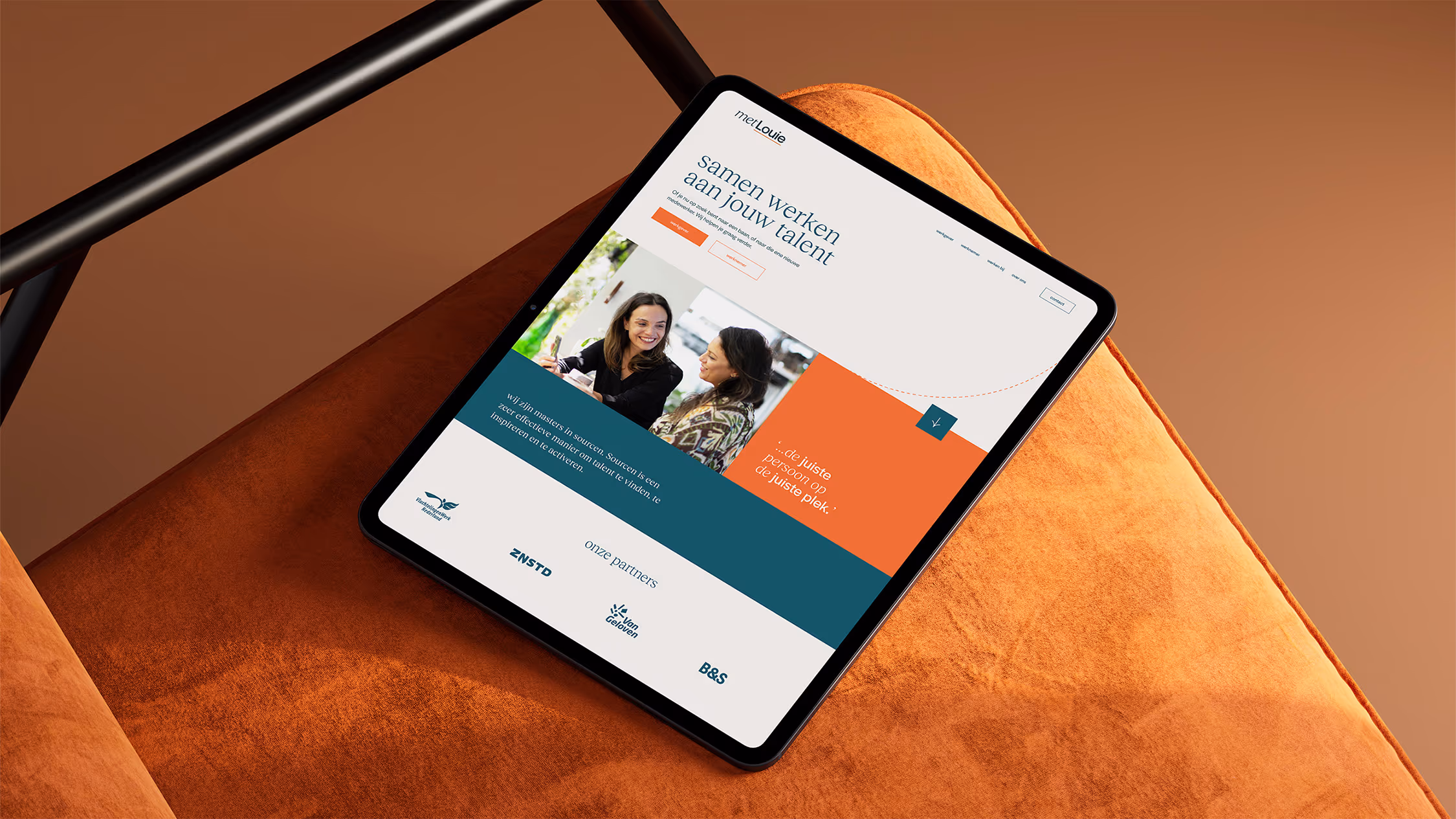 Tablet displaying a website with a header in Dutch, an image of two women talking, and sections in blue and orange on an orange fabric surface.