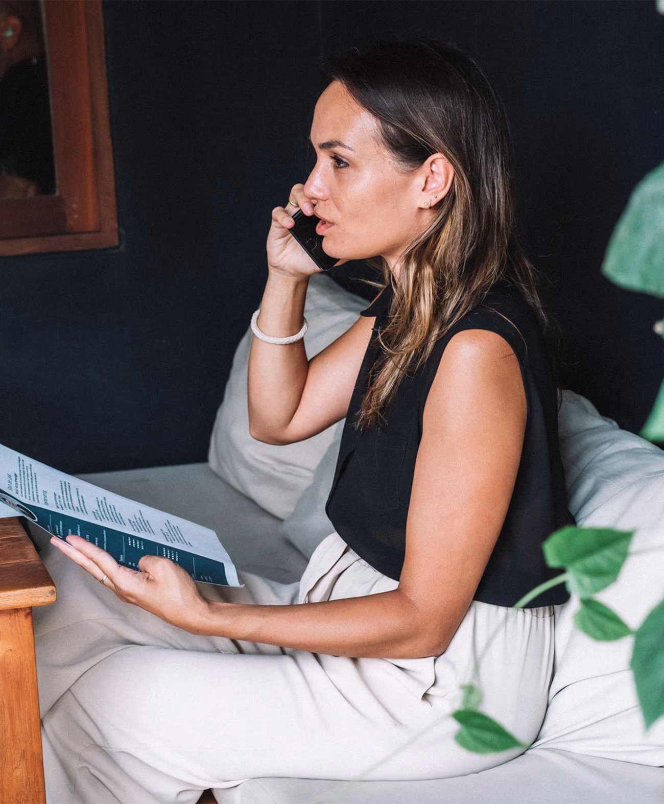 Woman sitting on a couch holding a menu and talking on a smartphone.
