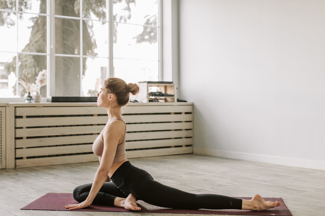 Free A Woman Stretching Her Leg while Sitting on a Yoga Mat Stock Photo