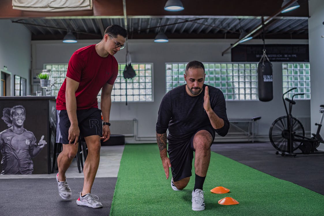 Free Full body of focused man in sportswear doing stretching exercises with coach in contemporary fitness center Stock Photo