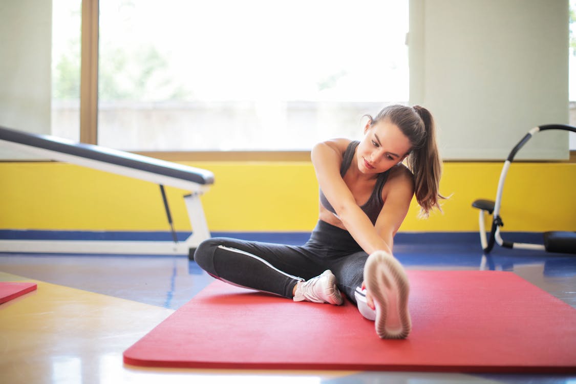 Free Woman in Black Sports Bra and Black Legging Sitting on Red Yoga Mat Stock Photo