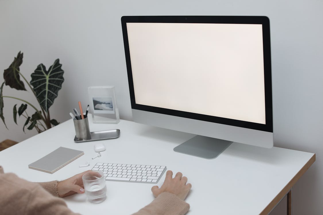 Free Crop anonymous person in sweater sitting at table with glass of water while working at computer Stock Photo