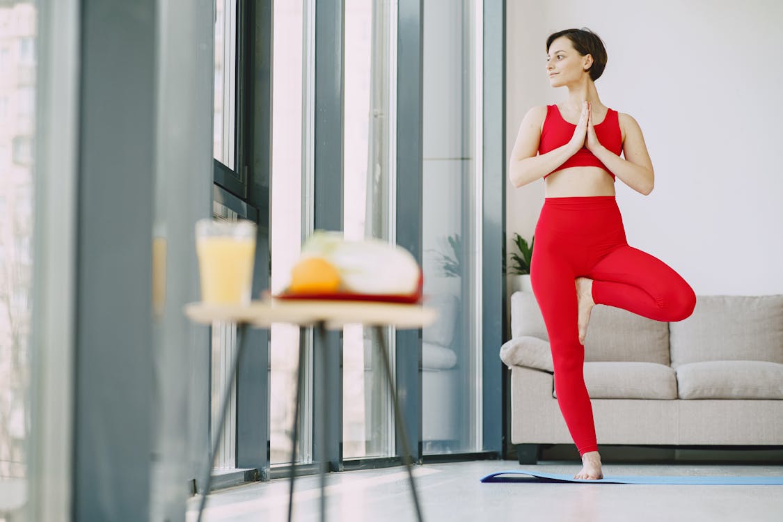 Free From below of content female in activewear standing on mat in living room while doing yoga exercise and looking away Stock Photo
