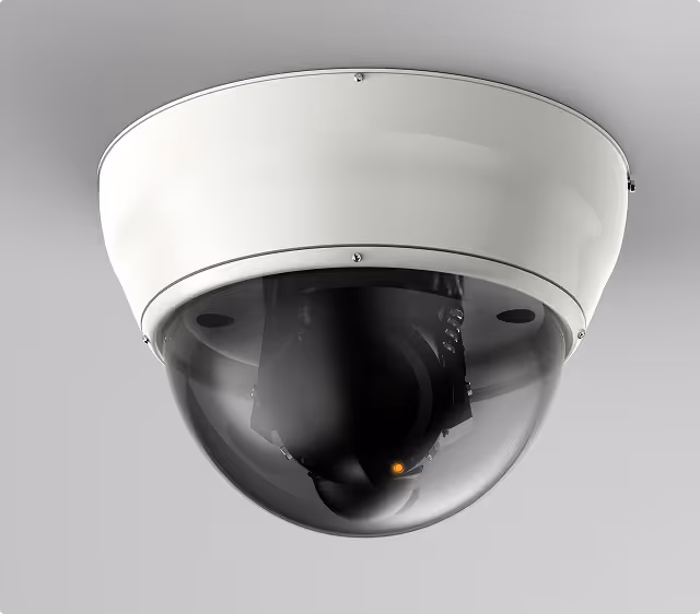 White dome security camera mounted on a ceiling with a dark tinted cover and a small orange indicator light.