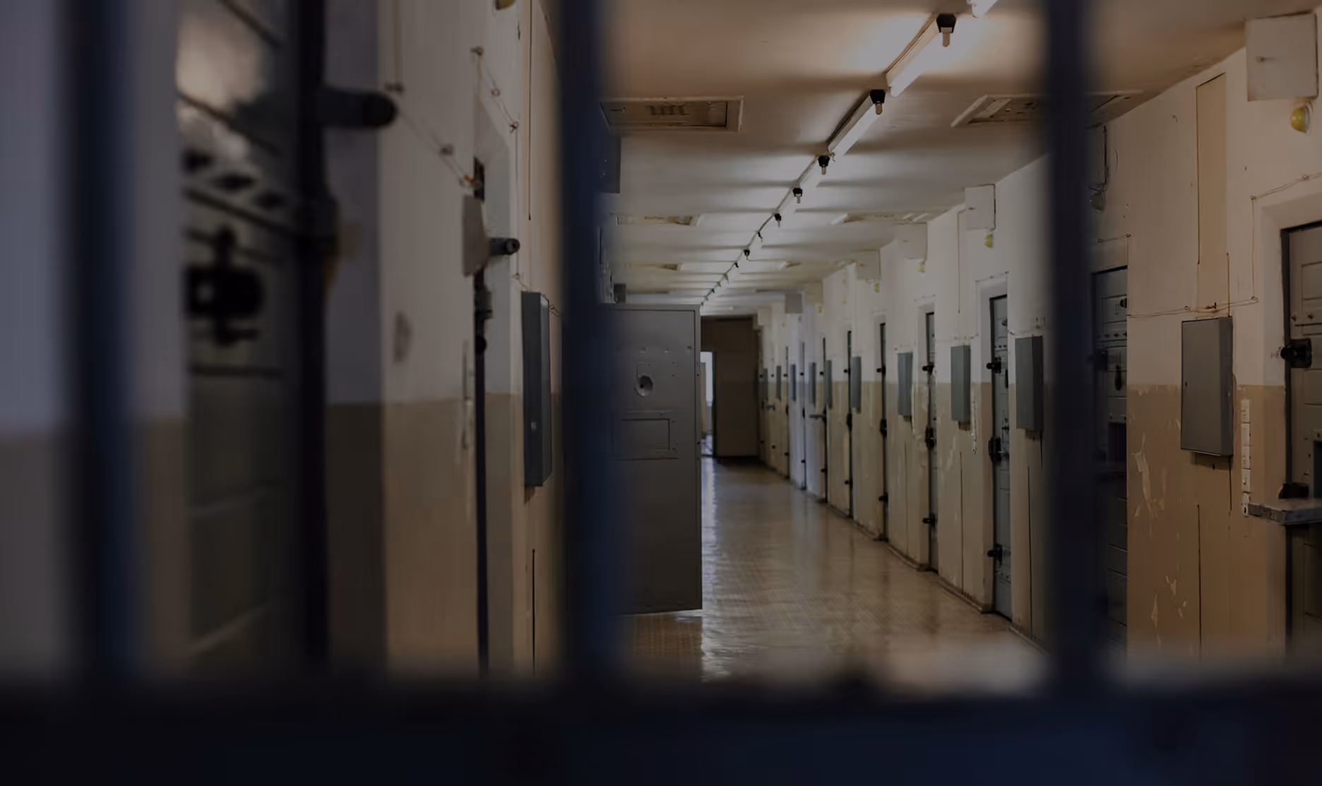 Empty corridor in a prison with closed cell doors on both sides and one door slightly open.