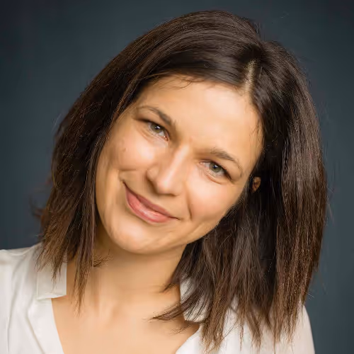 Vrouw met halflang bruin haar lacht vriendelijk tegen een neutrale achtergrond.