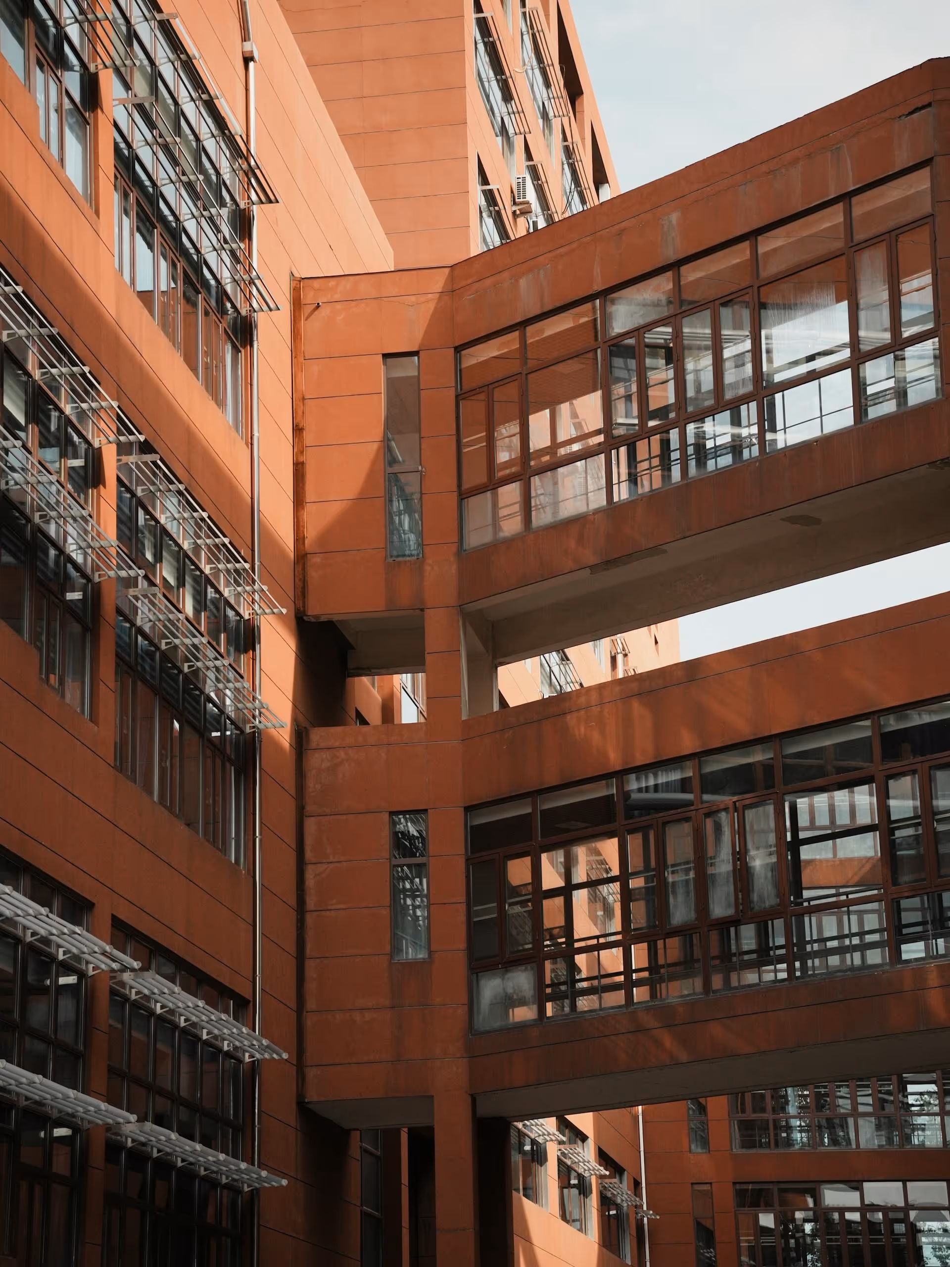 Bâtiment d'entreprise moderne avec passerelles en verre entre des sections en brique rouge.