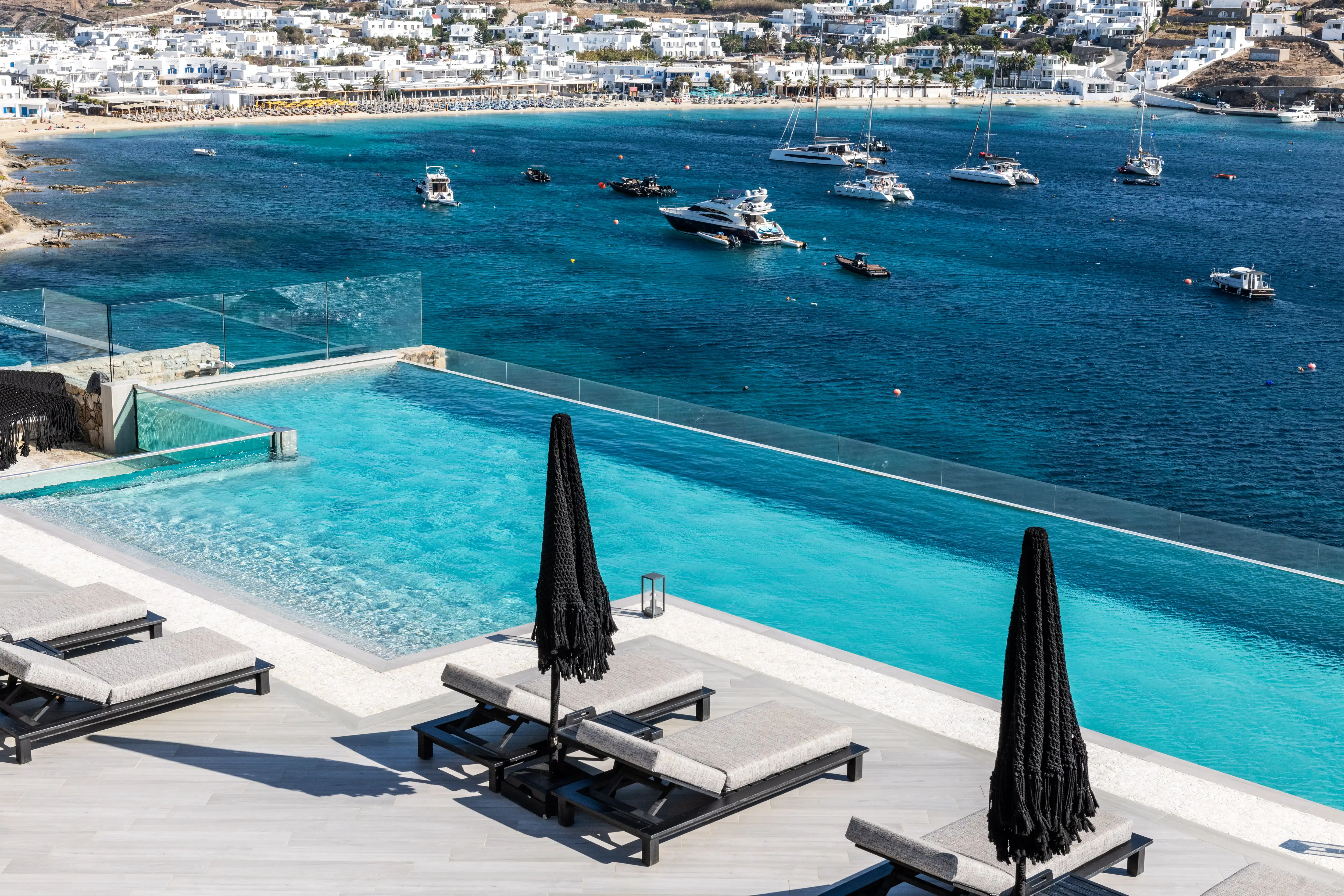 Three pairs of sunbeds infront of the infinity pool overalooking the sea and Mykonos.