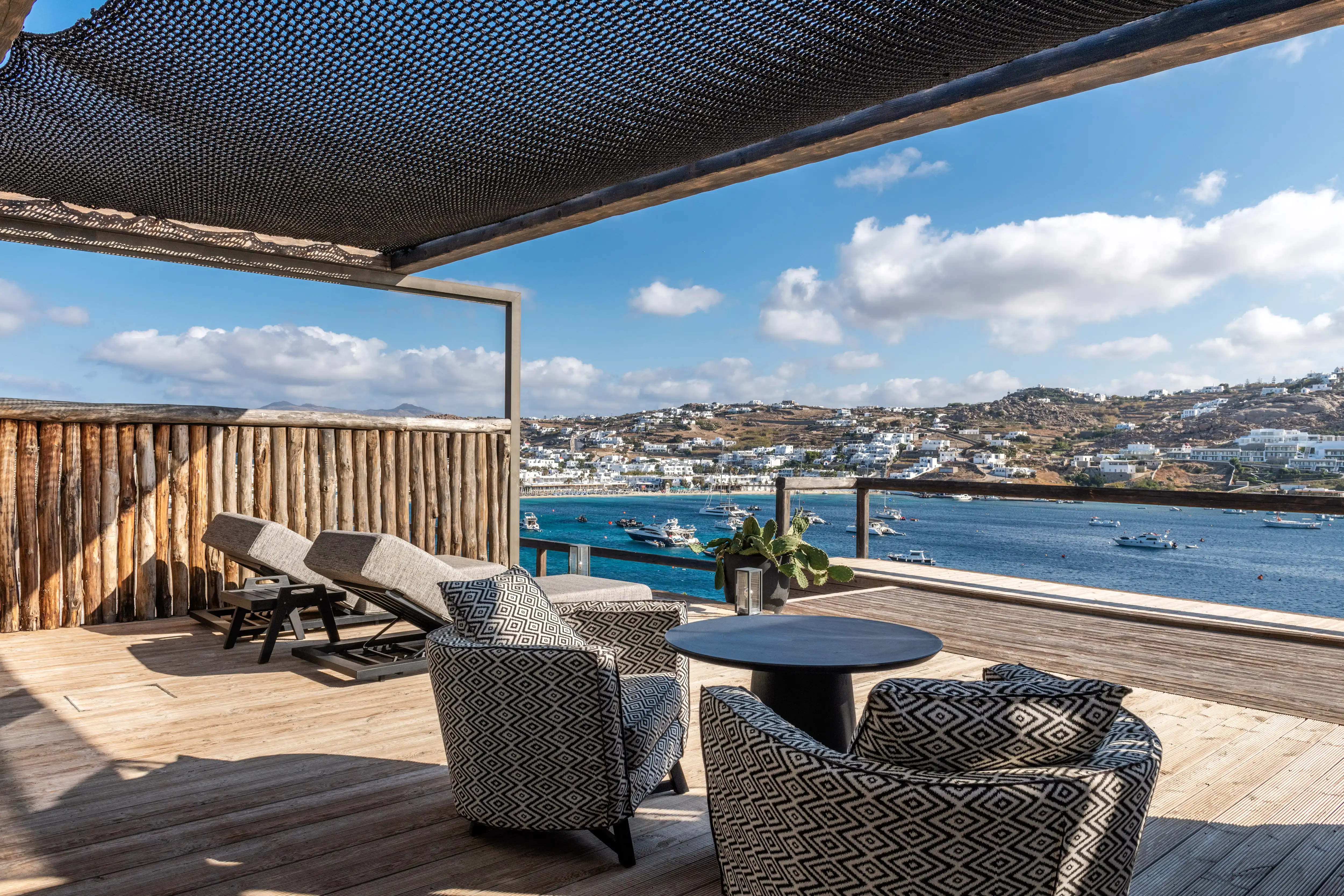 A set of chairs and sunbeds on a wooden deck, overlooking Mykonos.