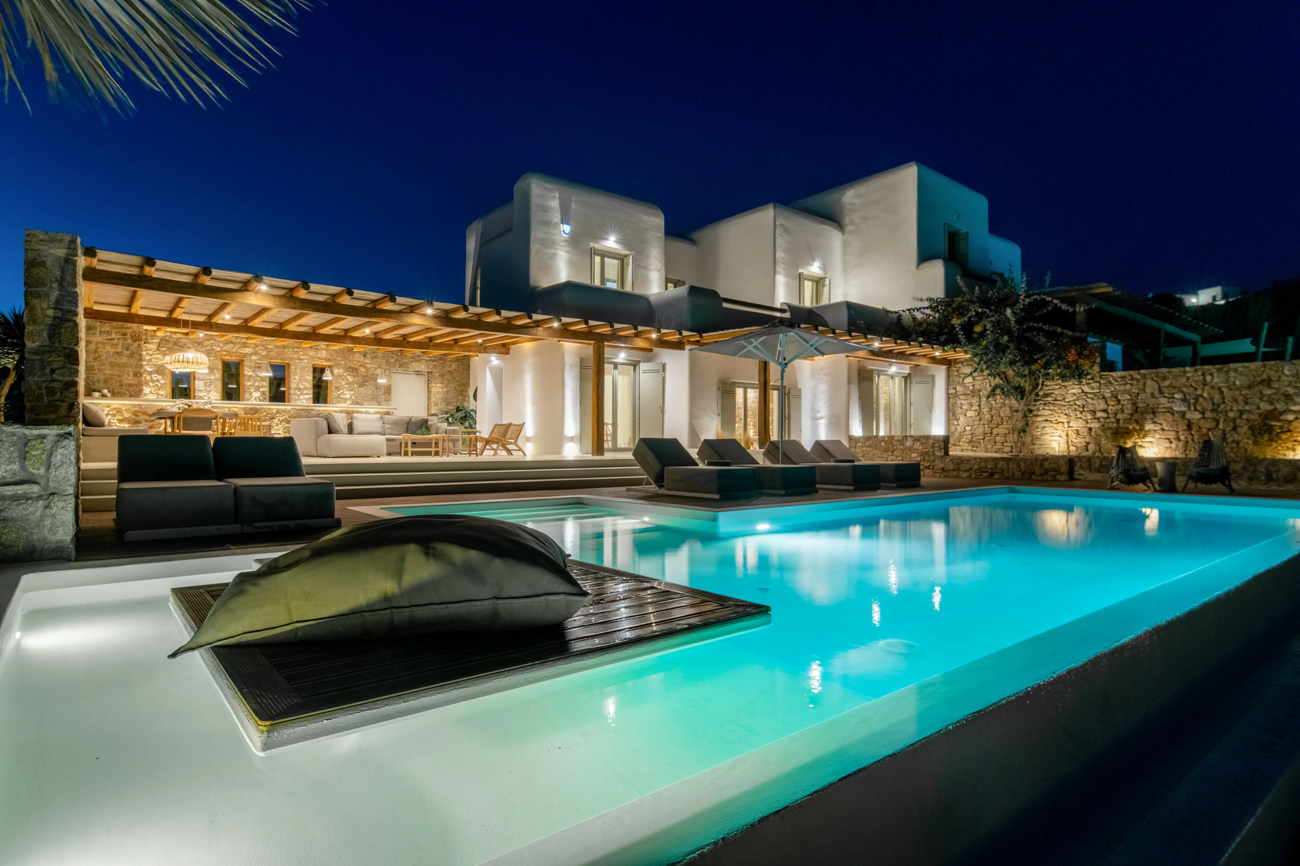 A lighted pool in front of a villa.