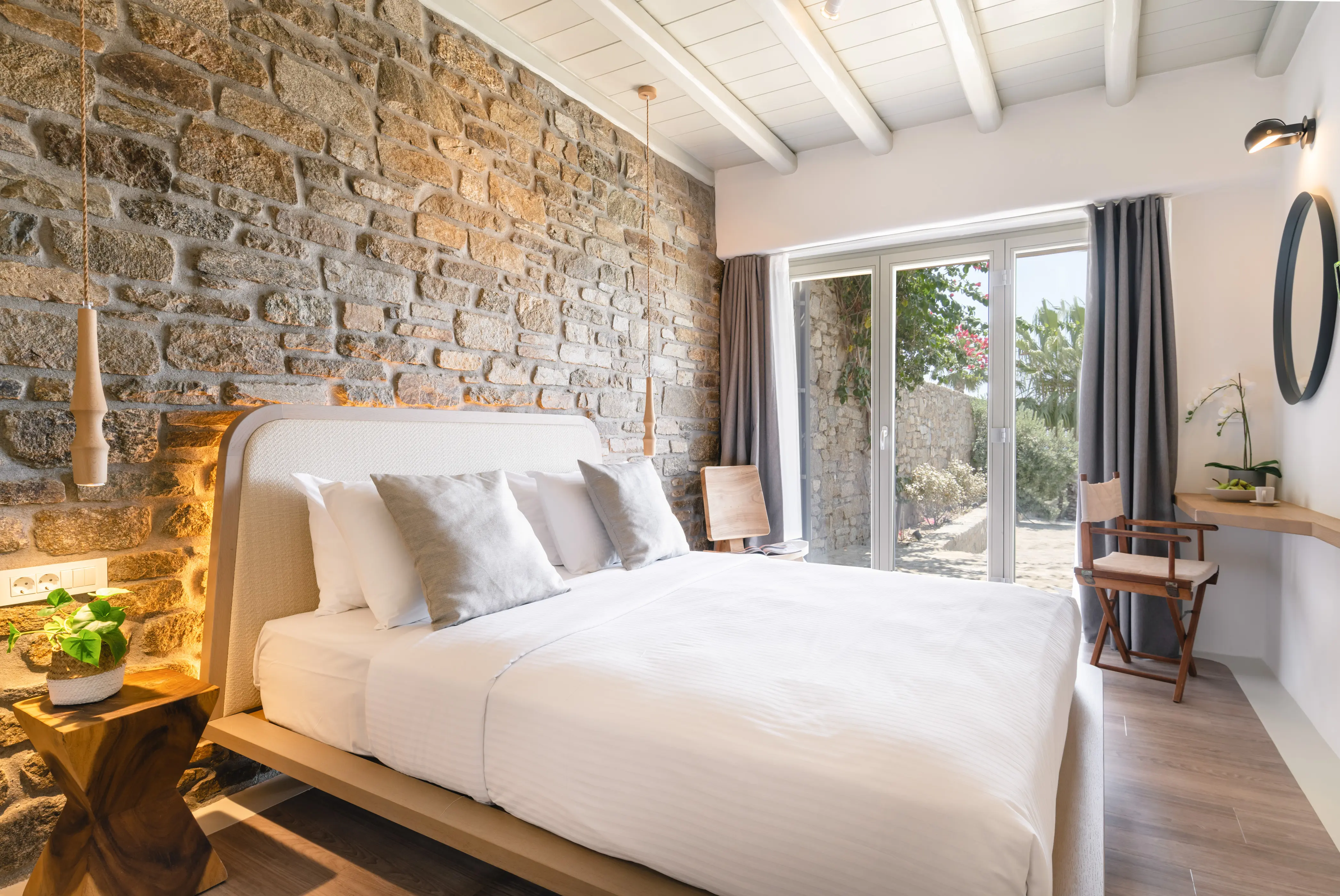 A double bed in front of a stone wall and a big window.