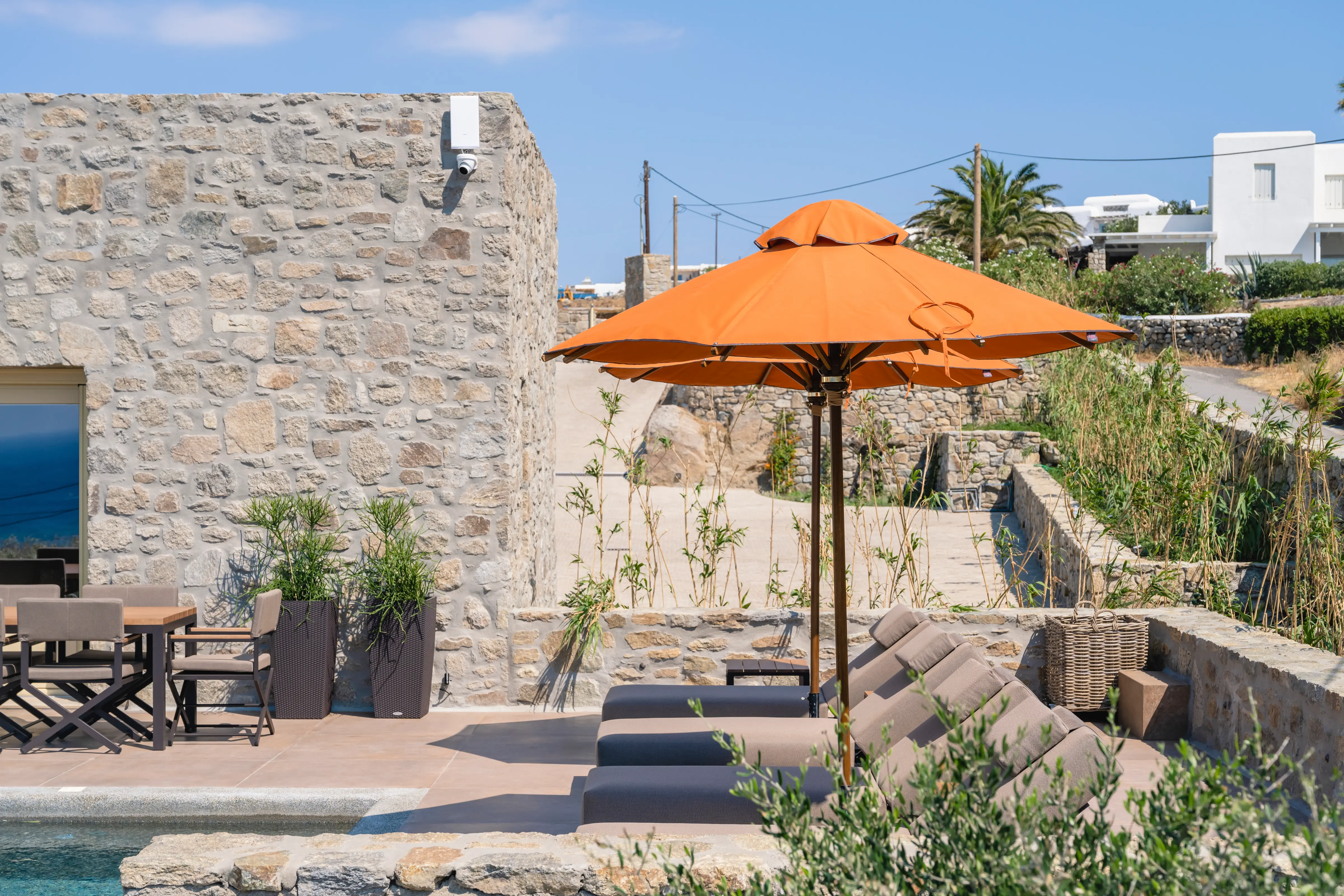 A pair of orange umbrellas, over sunbeds, next to the stone villa.