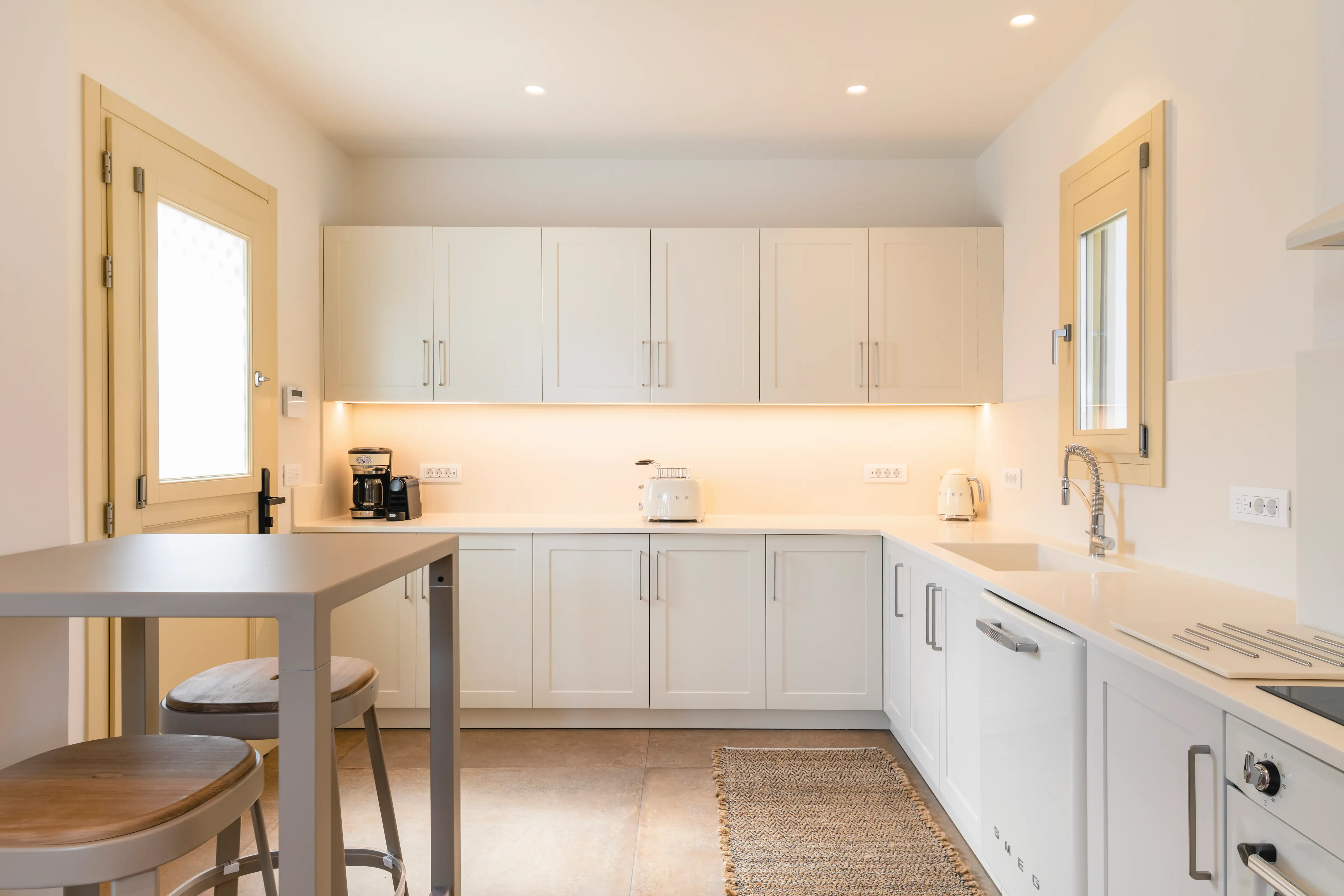 A kitchen with a tall table on the left, and white cupboards.