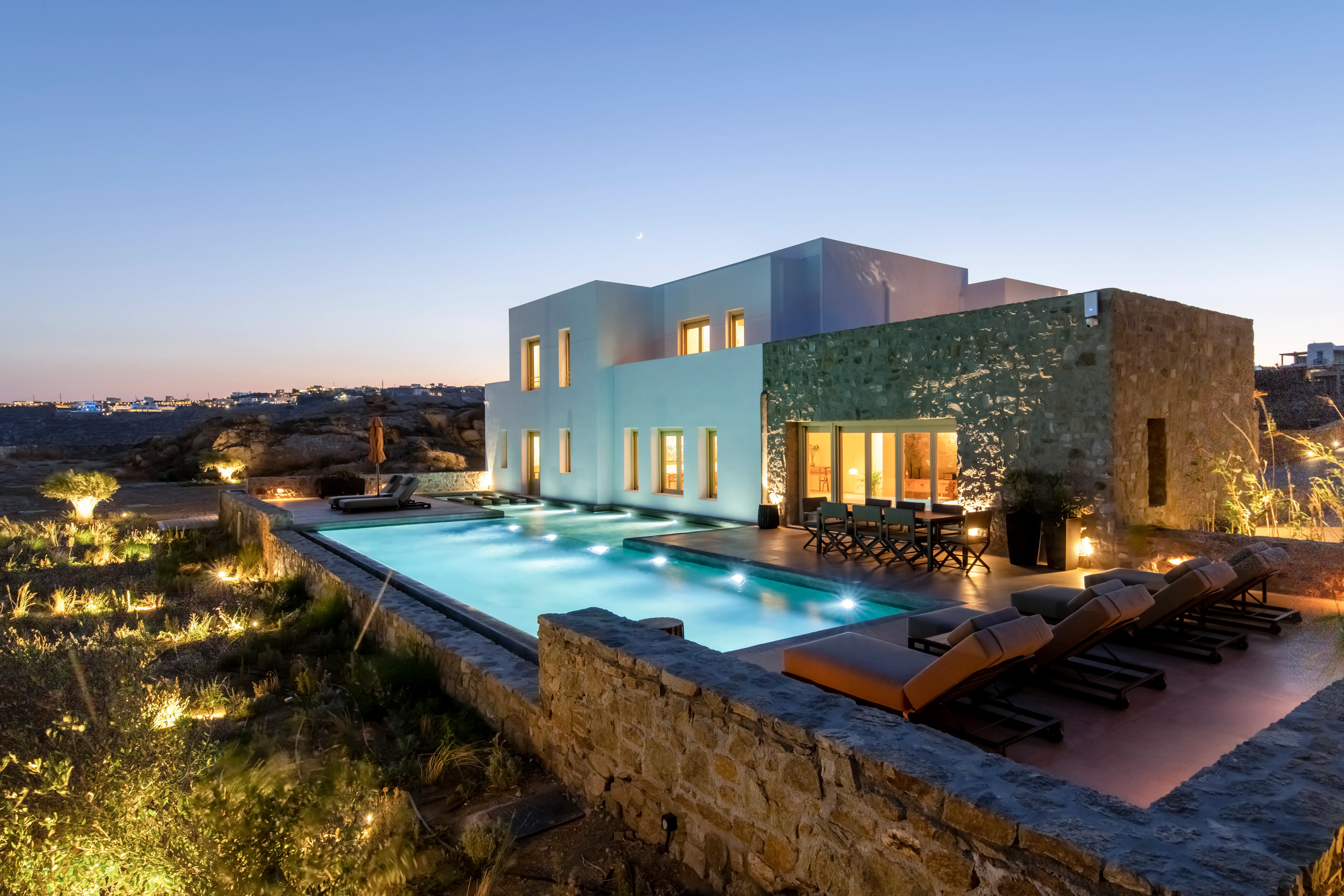 A lighted pool in front of a white and stone villa.