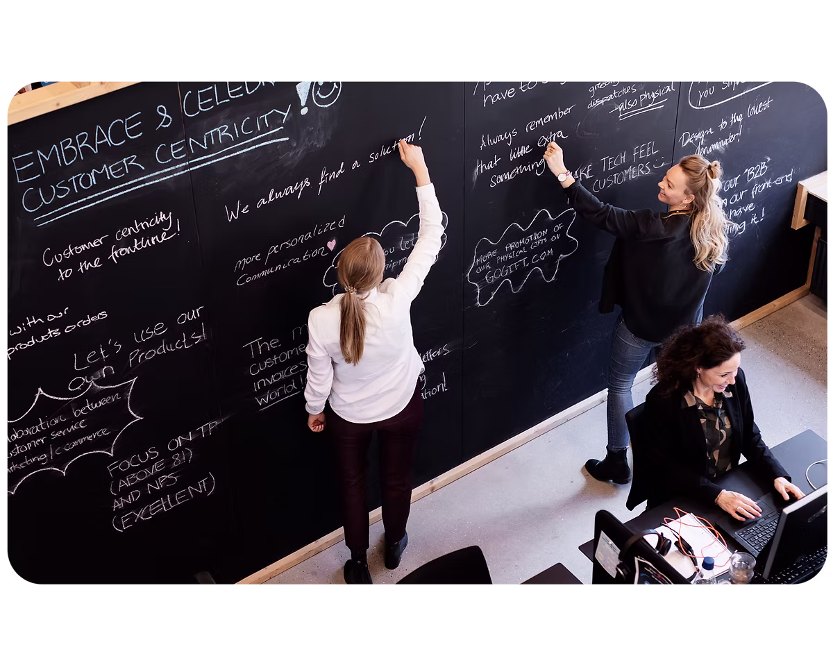 Team members writing ideas on a large chalkboard during a customer-centricity brainstorming session