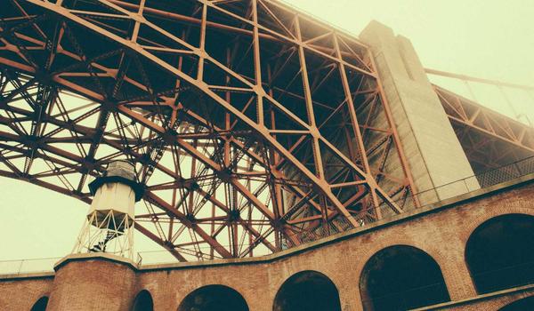 Photo looking up at the underside of a steel truss bridge with a brick archway