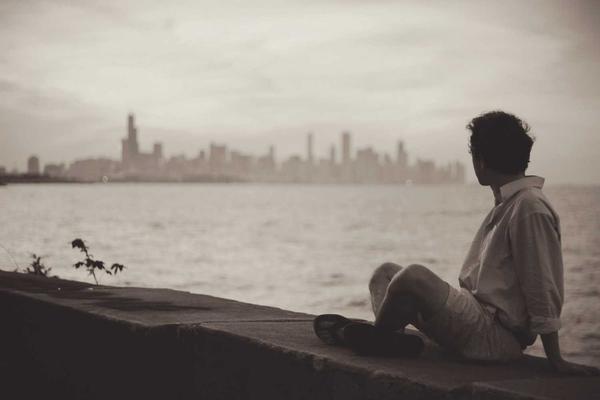 Sepia-toned photo of a person sitting on a ledge looking out at a city skyline across water