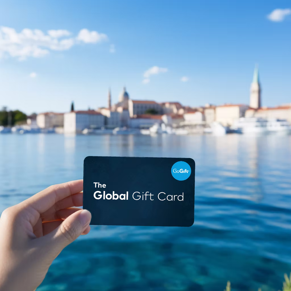 Hand holding The Global Gift Card in front of a coastal town in Croatia