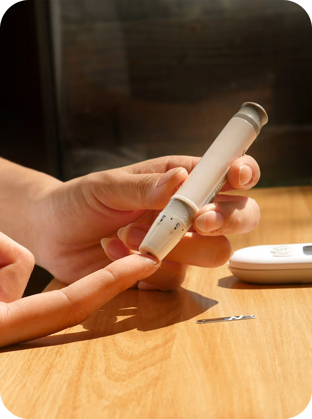 Person using a lancet device to prick their finger for a blood glucose test on a wooden table.