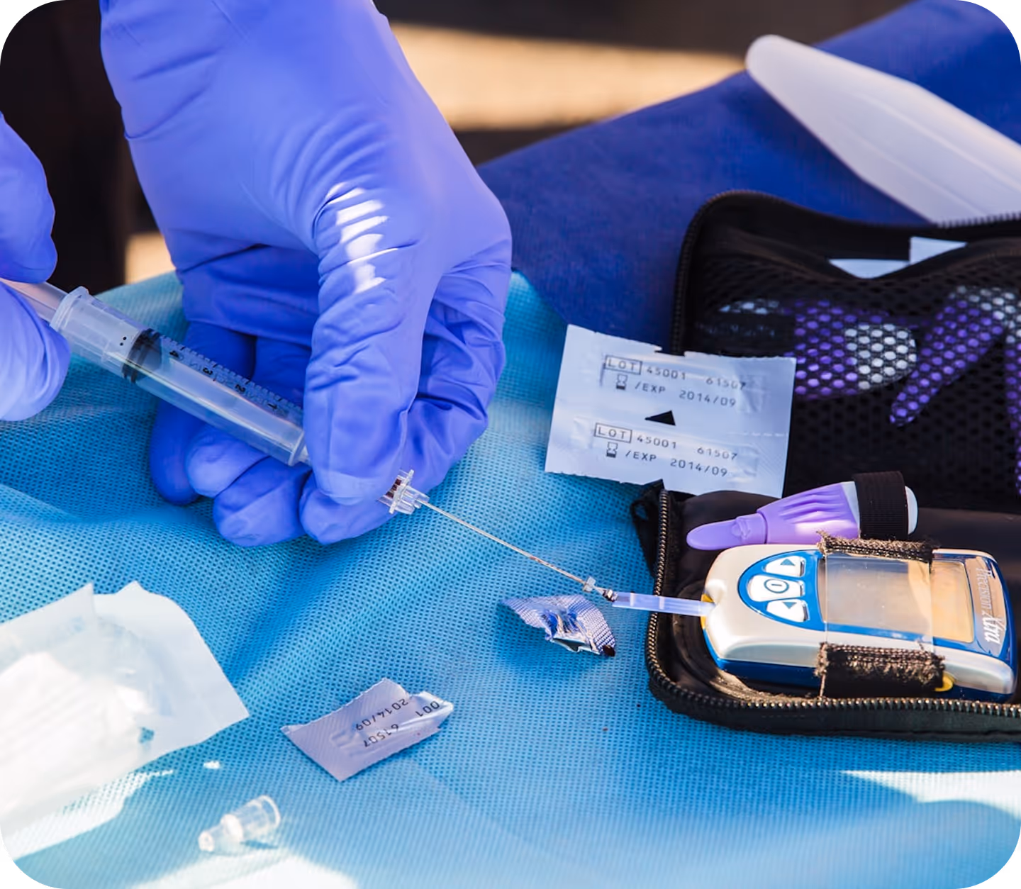 Gloved hands holding a syringe preparing to draw blood from a glucose meter test strip on a blue medical drape.