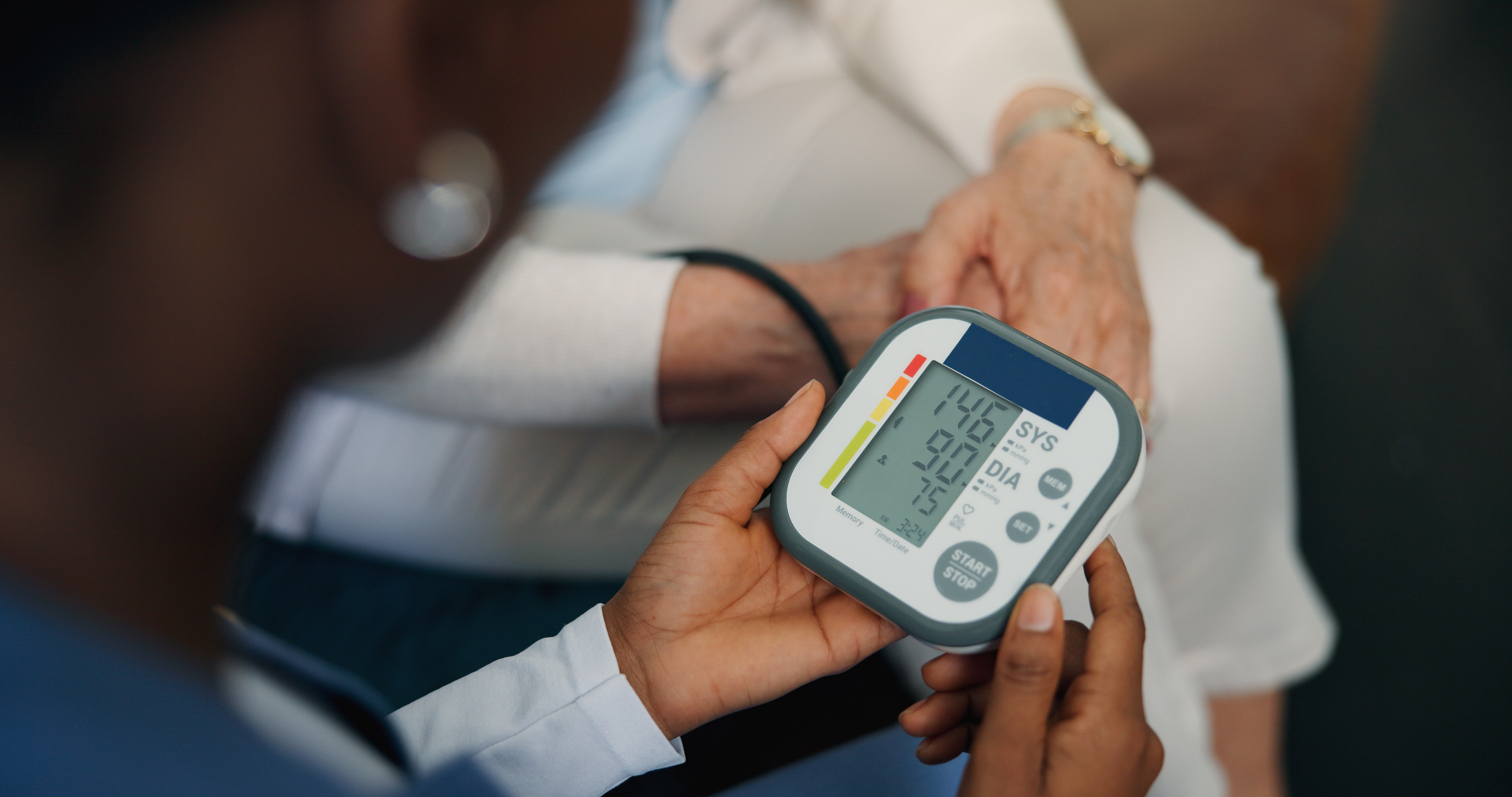 Healthcare professional holding a digital blood pressure monitor displaying a reading of 146/90 mmHg on an elderly person's arm.