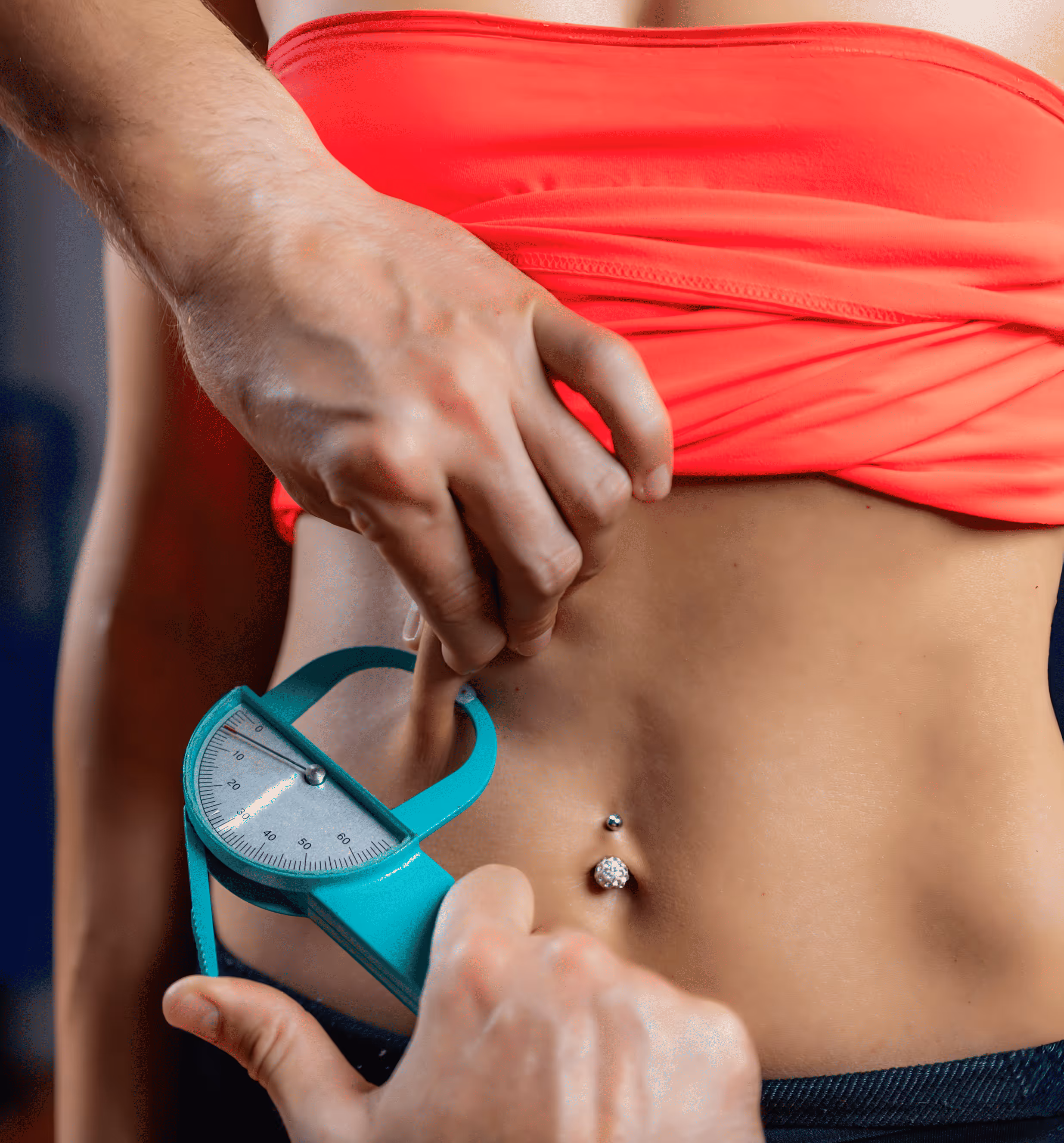 Person using a caliper to measure skinfold thickness on a woman’s bare abdomen wearing a red top.
