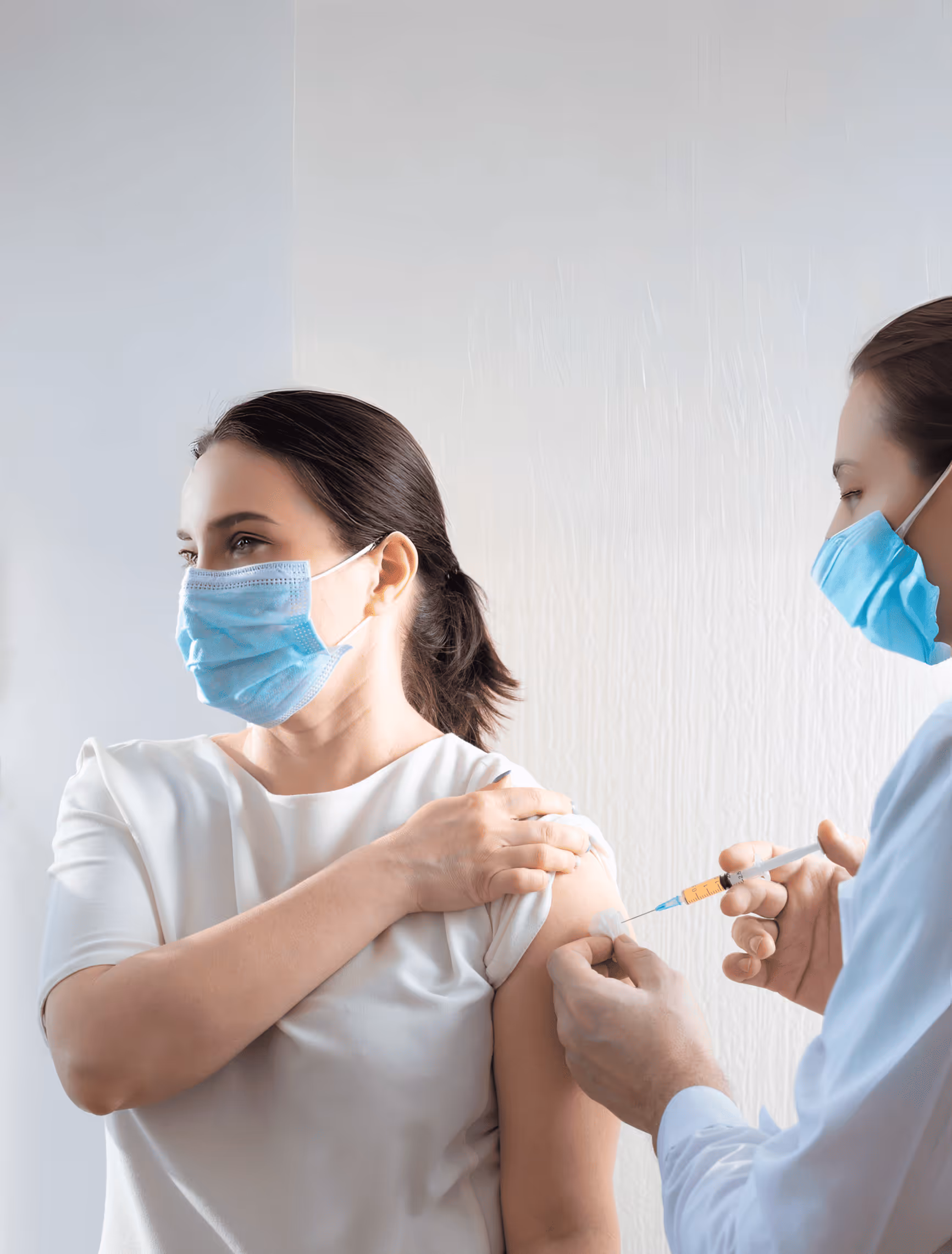 Healthcare professional wearing a mask administering a vaccine injection to a masked woman’s upper arm.