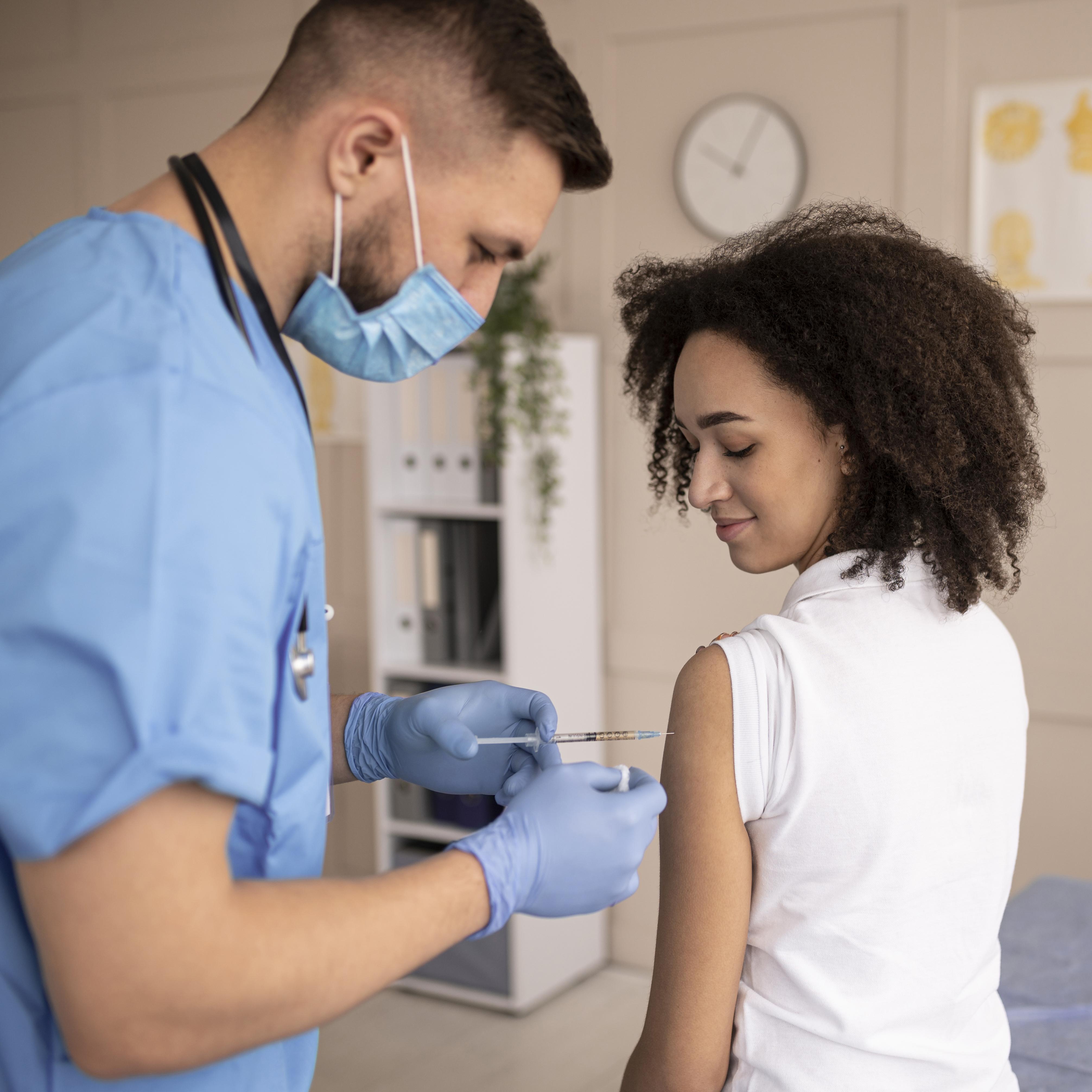 Healthcare professional wearing mask and gloves administering vaccine injection to a smiling woman in a clinic.
