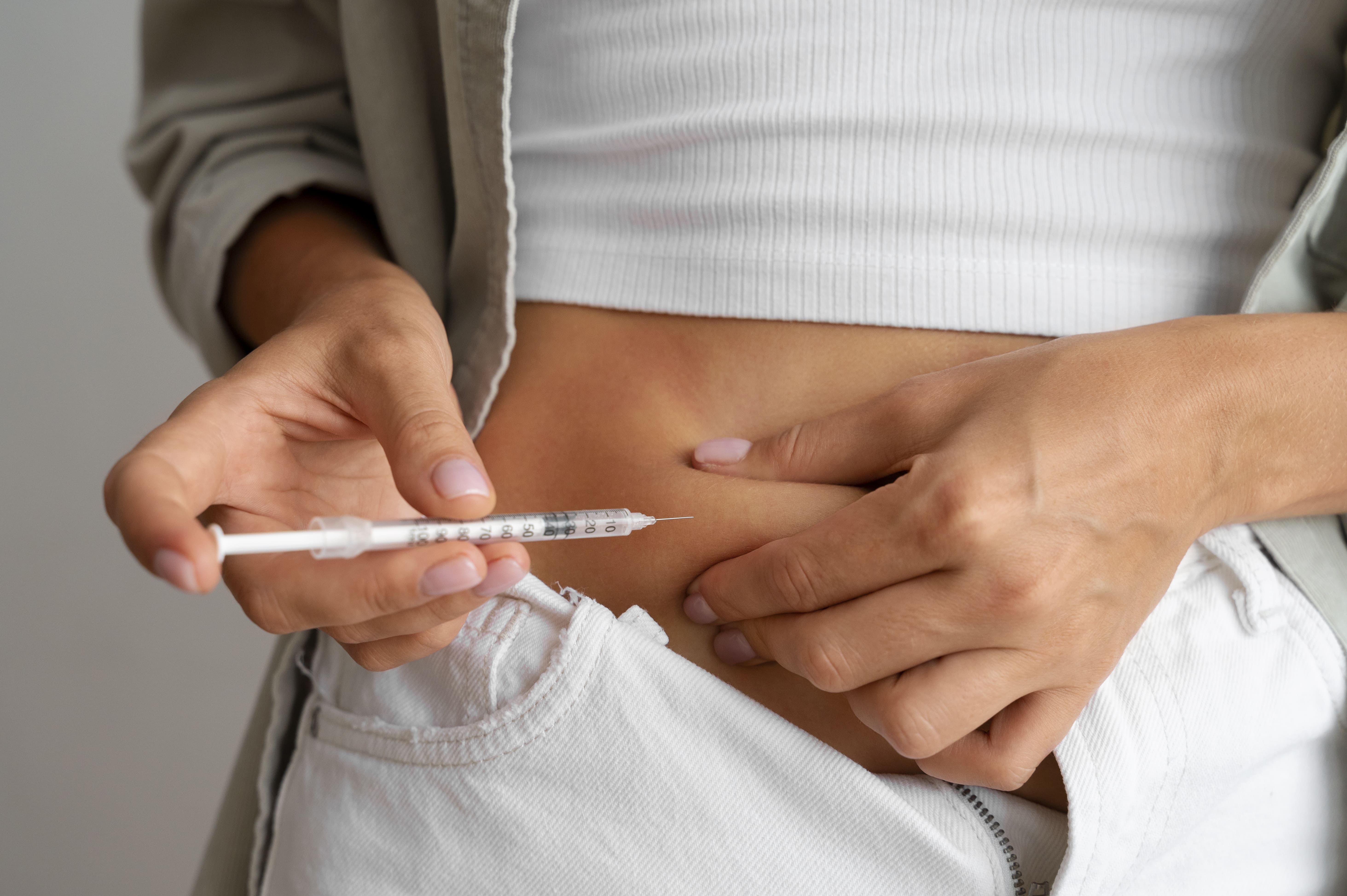 Person preparing to inject insulin into their abdomen with a syringe.
