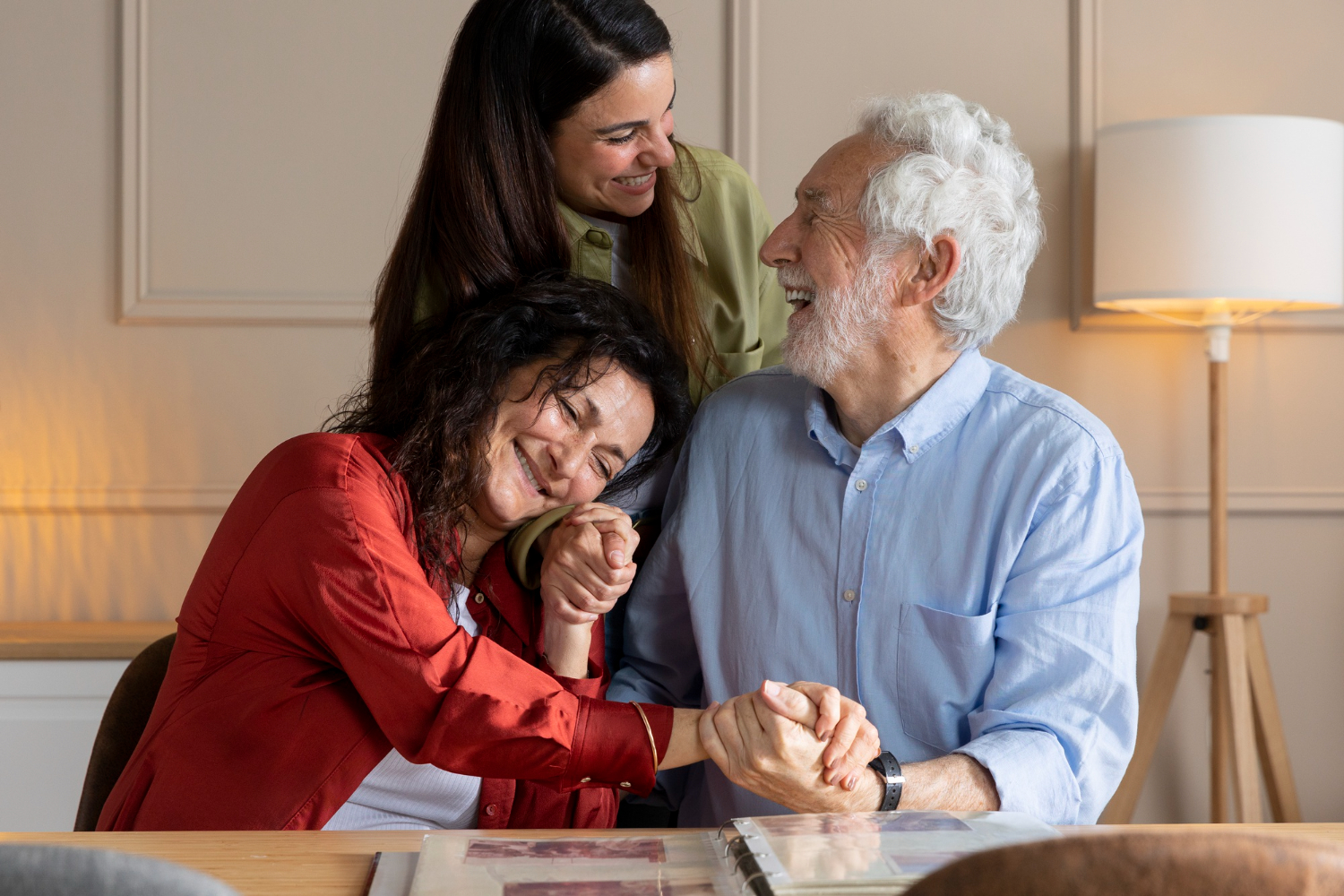 Three people smiling and holding hands around a table with photo albums.