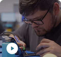 Man wearing glasses focused on soldering an electronic component on a circuit board.