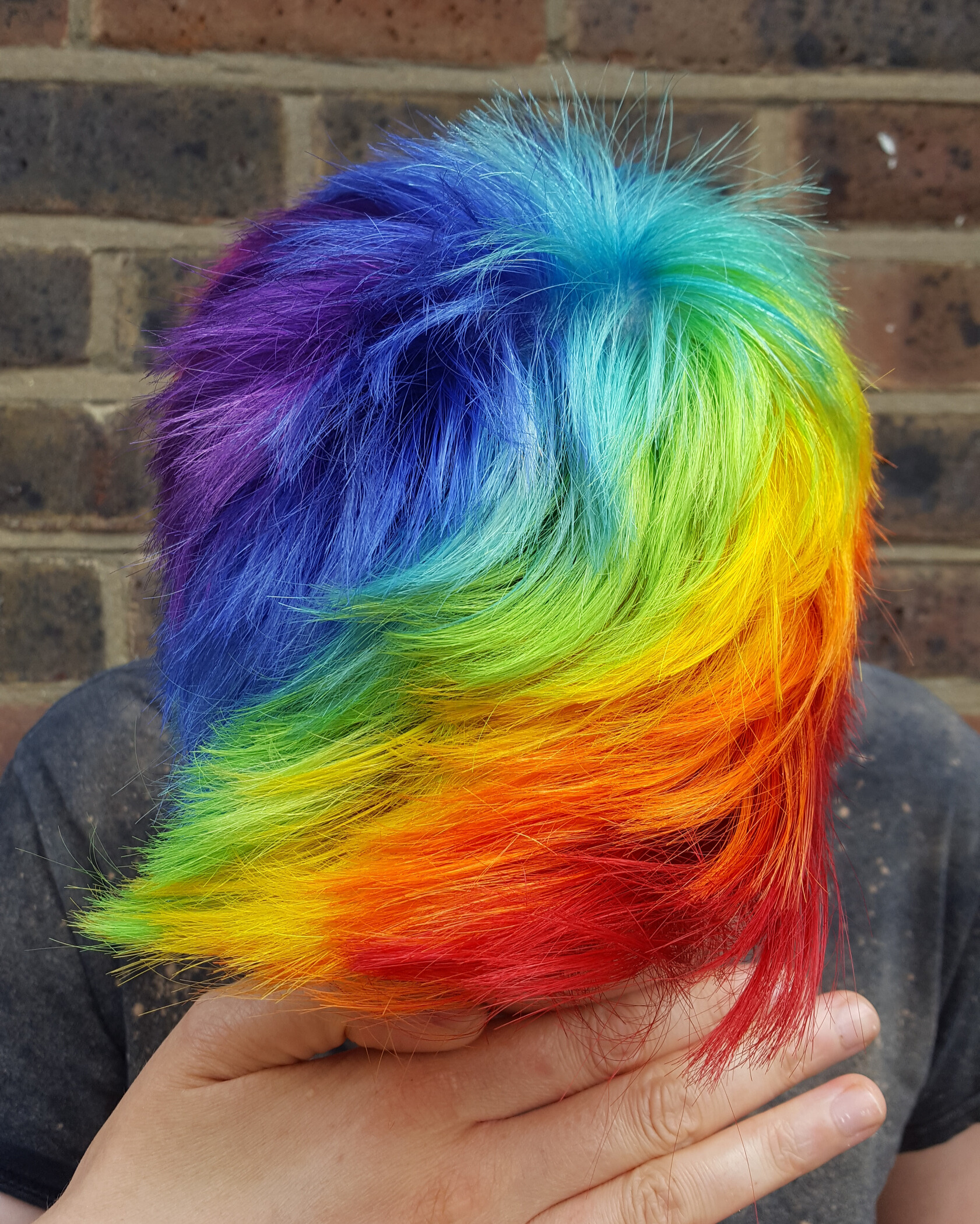 Person with short hair dyed in vibrant rainbow colors covering their face with their hand.