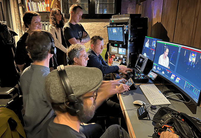 Ein Team von sieben Personen arbeitet gemeinsam in einem Kontrollraum mit mehreren Bildschirmen, die Live-Videoaufnahmen und Steuerungssoftware anzeigen.