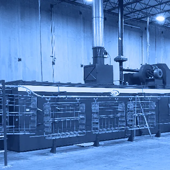 Large blue industrial parts washer with metal racking and safety guard rails inside a warehouse facility.