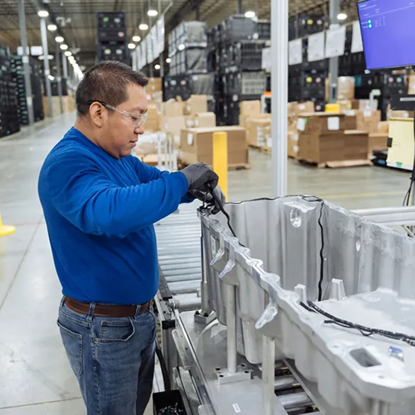 Worker in safety glasses installing wiring harness inside a large metal housing at an assembly workstation.