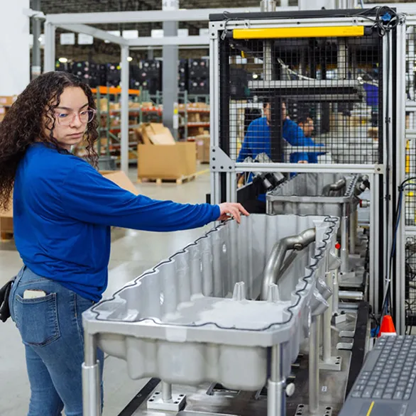 Worker in blue shirt positioning a large metal component in a test fixture on an assembly line.