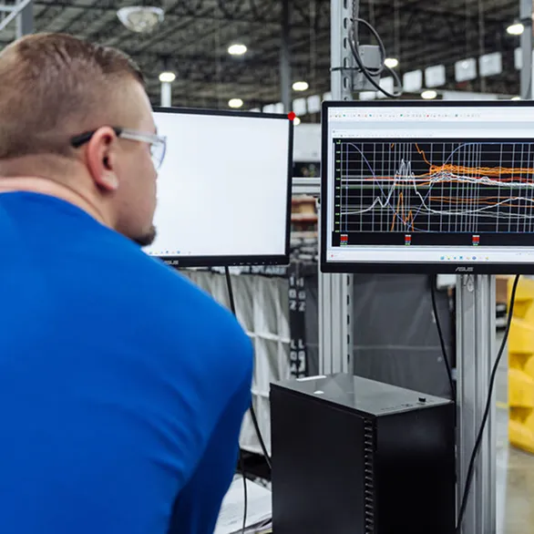 Worker views performance graphs on a computer monitor while standing at a test station on the assembly line.