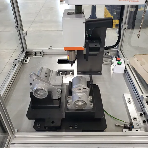 Interior view of an automated marking station with cast components clamped in a fixture, push-button controls mounted on the right side panel.