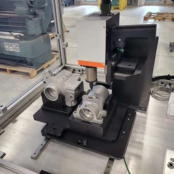 Close-up of two cast metal housings secured in a black fixture beneath a vertical marking head inside a safety enclosure.