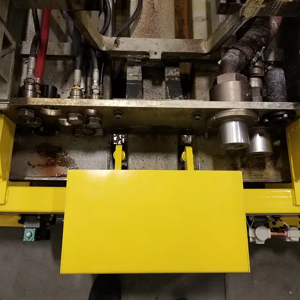 Close-up view of a yellow docking fixture secured beneath a large industrial assembly with visible hydraulic lines and metal housings.