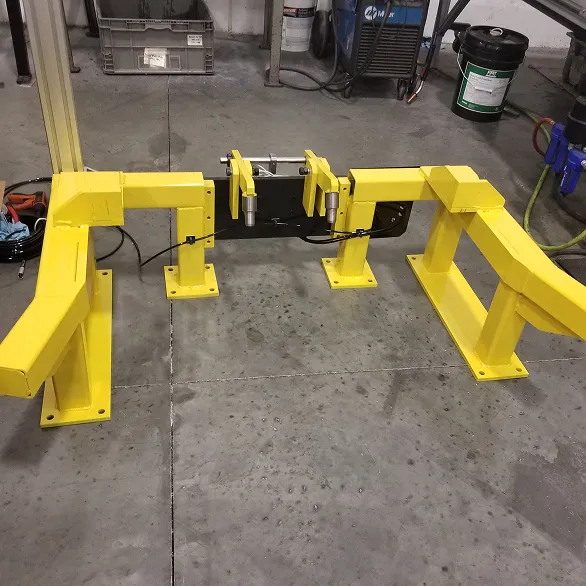 Yellow steel docking fixture with four floor-mounted supports and adjustable clamping arms positioned on a concrete shop floor.