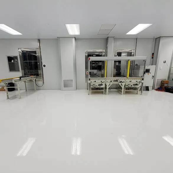 Wide view of a clean room with white epoxy flooring, overhead lighting, a conveyor line, and enclosed automation equipment along the wall.