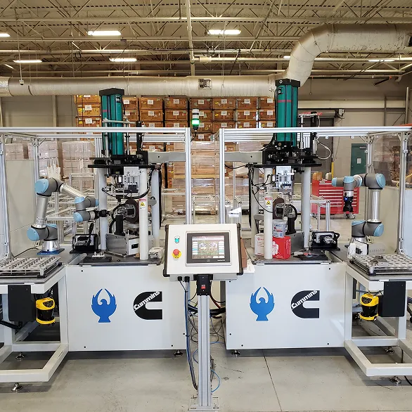Wide view of a dual-station automated cell with two collaborative robotic arms, vertical presses, fixture tables, and a central control panel inside a factory environment.