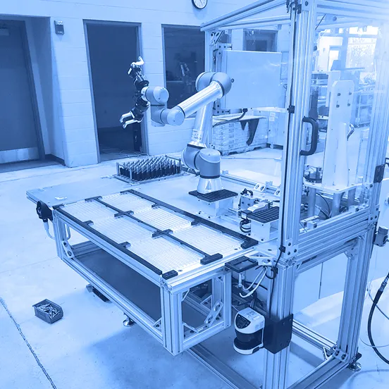 Collaborative robotic arm mounted above a worktable with fixtures and trays inside a guarded inspection cell on a factory floor.