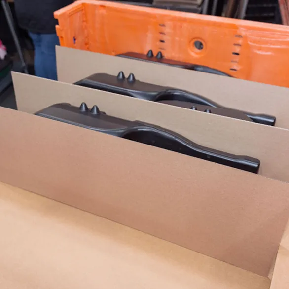 Black plastic parts separated by cardboard divider inserts inside an orange plastic returnable tote.