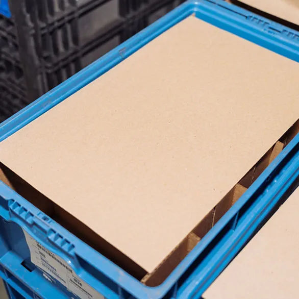 Flat cardboard liner placed on top of a compartment divider insert inside a blue plastic returnable tote.